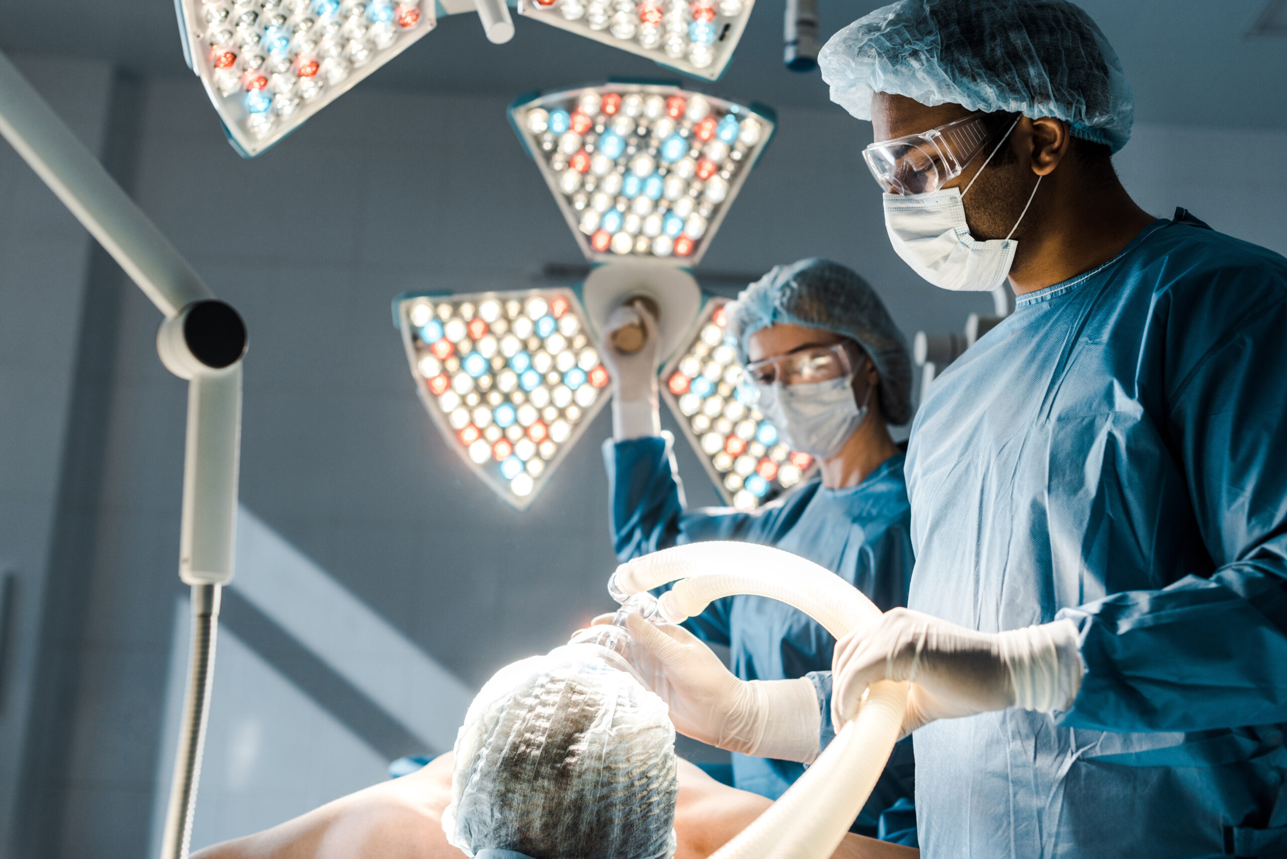 selective focus of surgeon in uniform and medical cap putting mask on patient